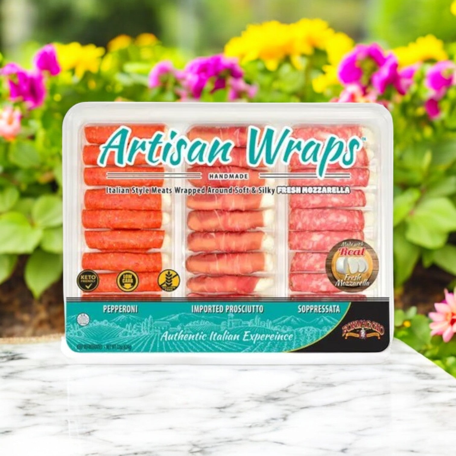 A 22 oz package of Formaggio Artisan Wraps with cured meats and mozzarella cheese, marked "Keto Friendly" and offering an "Authentic Italian Experience," is set on a table decorated with colorful flowers.