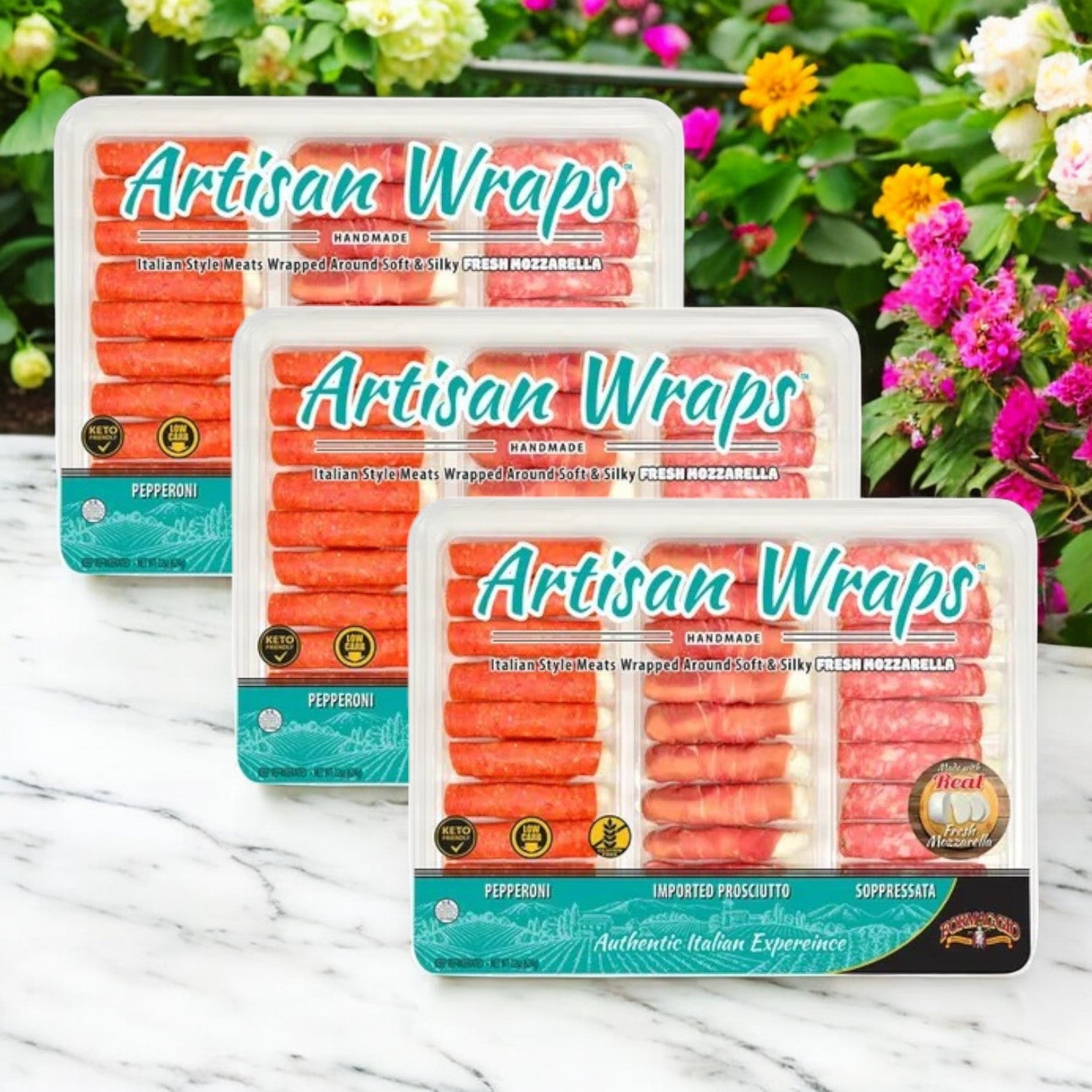Three Formaggio Artisan Wraps, 22 oz. - 3 Count, filled with gourmet snacks like pepperoni, prosciutto, soppressata, and mozzarella cheese are displayed in front of vibrant flowers.
