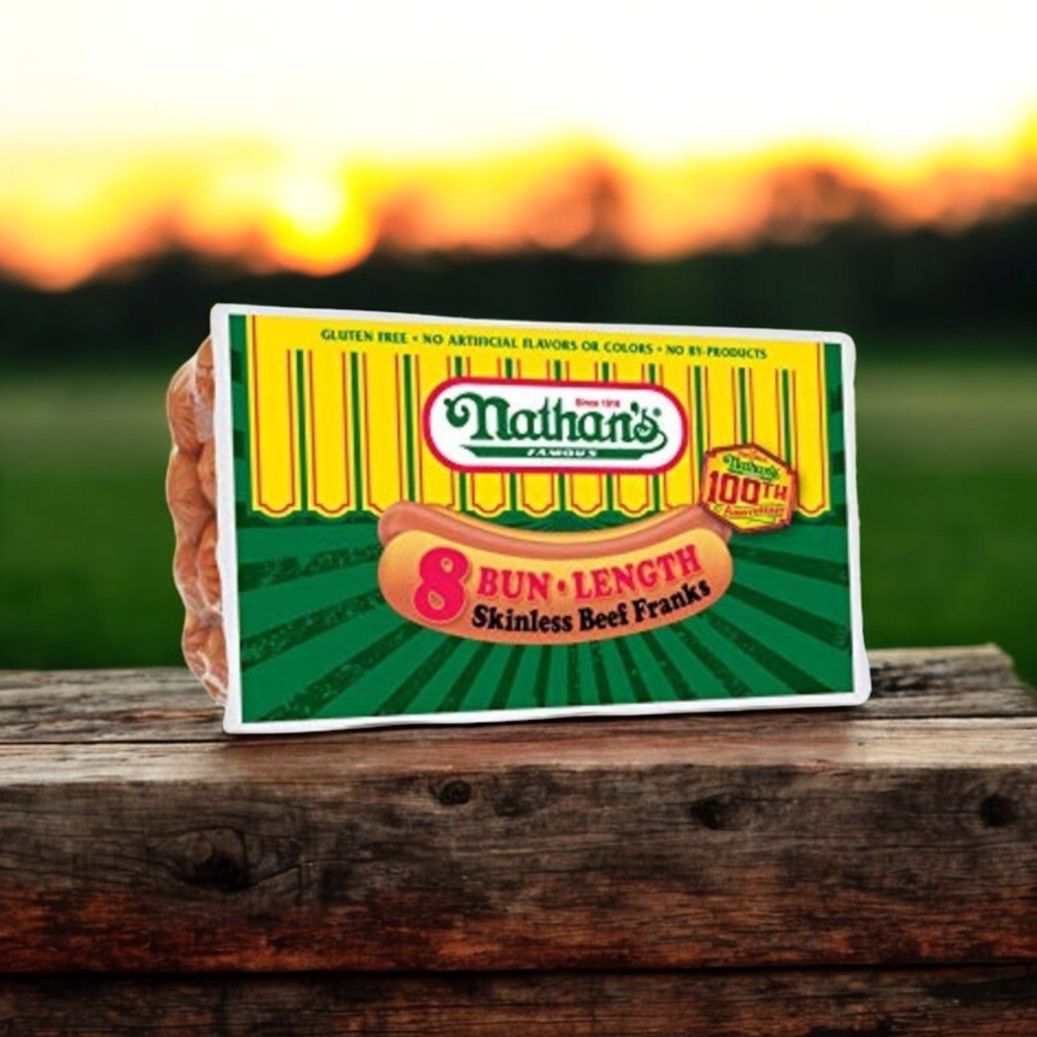A package of Nathan’s Famous 8" Bun Length Beef Franks, a premium all-beef hot dog, rests on a wooden surface against a sunset backdrop.