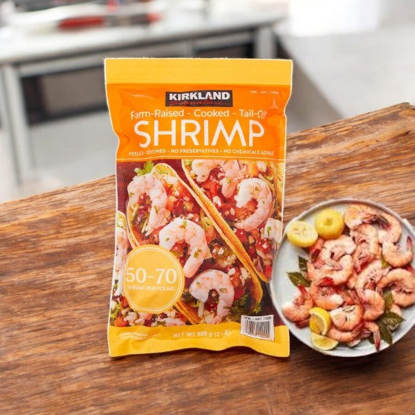 A bag of Kirkland Signature Farm-Raised Cooked Shrimp, peeled and deveined (50-70 count, 2 lbs), rests on the counter beside a bowl of cooked shrimp with lemon slices.