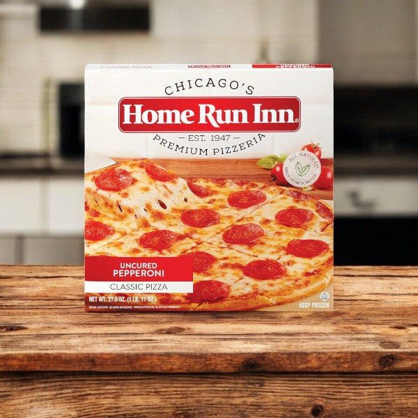 A box of Home Run Inn Classic Pizza, Uncured Pepperoni, 27 oz. - 1 Count sits on a wooden kitchen surface, highlighting its homemade-style crust.