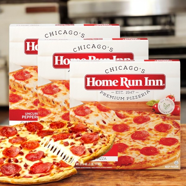 Three boxes of Home Run Inn Classic Pizza, Uncured Pepperoni, 27 oz. (3 total pizzas), are shown behind a homemade-style cooked pizza as a metal spatula lifts a hot, cheesy slice.
