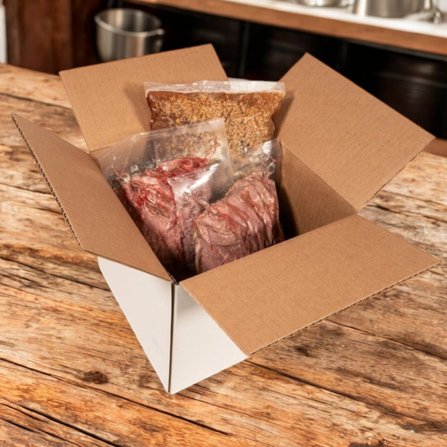 An open cardboard box on a wooden table displays vacuum-sealed packages containing Devanco's Devianco Foods Beef, Sliced Italian-Style with Gravy—10 lb pack (5 lb beef, 4 lb gravy).