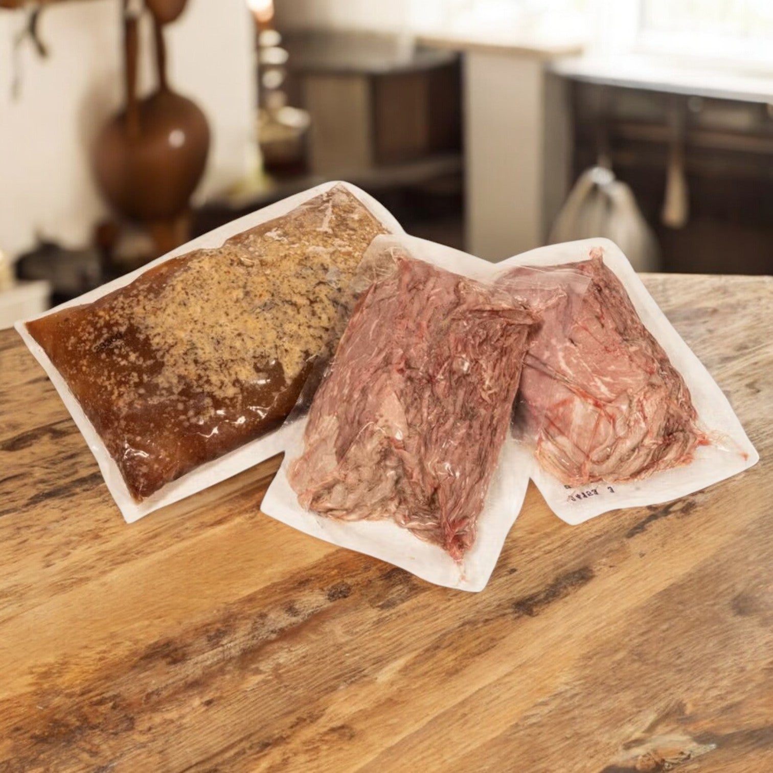 Three vacuum-sealed bags of Devanco's Devianco Foods Beef, Sliced Italian-Style with Gravy - 10 lb Package (5 lb Beef, 4 lb Gravy), are placed on a wooden kitchen counter with a blurry kitchen background.