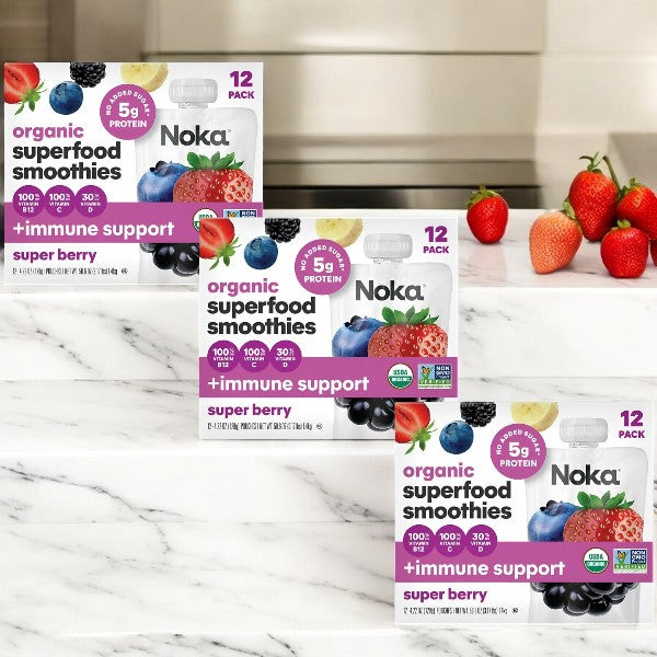 Noka Organic Super Berry Smoothies, 12-count (3 Packs) by Noka are on a marble counter, surrounded by strawberries and blueberries.