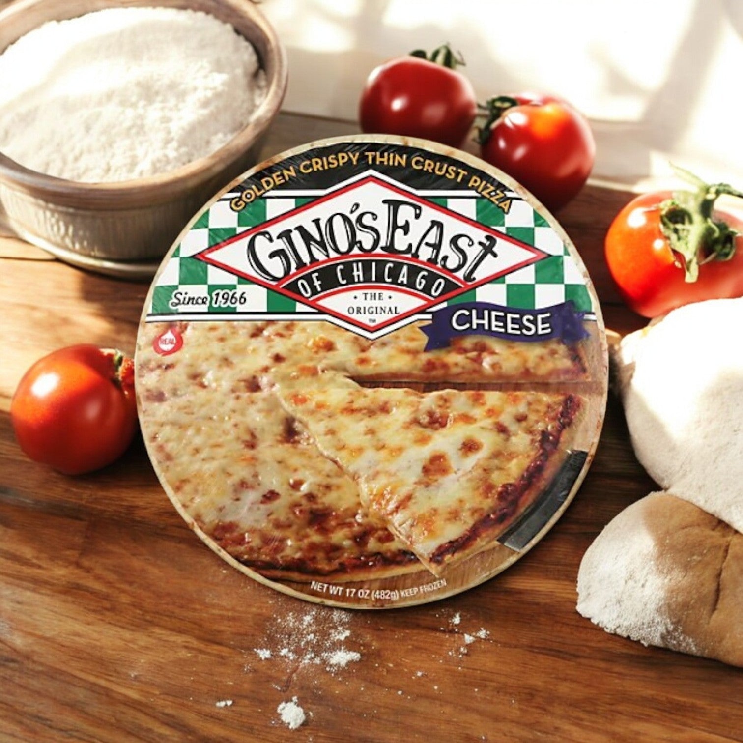Gino's East Pizza's Golden Crispy Thin Crust, 15.6 oz, rests on wood with tomatoes, flour bowl, and bread. Made in authentic Chicago style with rich mozzarella cheese for an irresistible traditional taste.