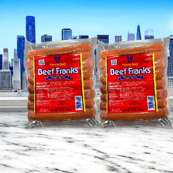 Two packs of Vienna Beef Frank Hot Dogs, 32 oz each, lie on marble with a city skyline in the background. Each pack offers Chicago-style hot dogs, ensuring authentic flavors in every bite.