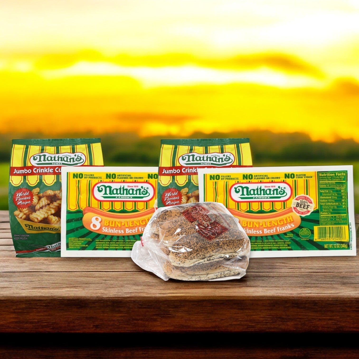The Nathan's Famous Hot Dog Bundle, featuring 16 hot dogs, 16 buns, and 2 bags of jumbo crinkle cut fries, is elegantly arranged against a sunset backdrop on a wooden surface.