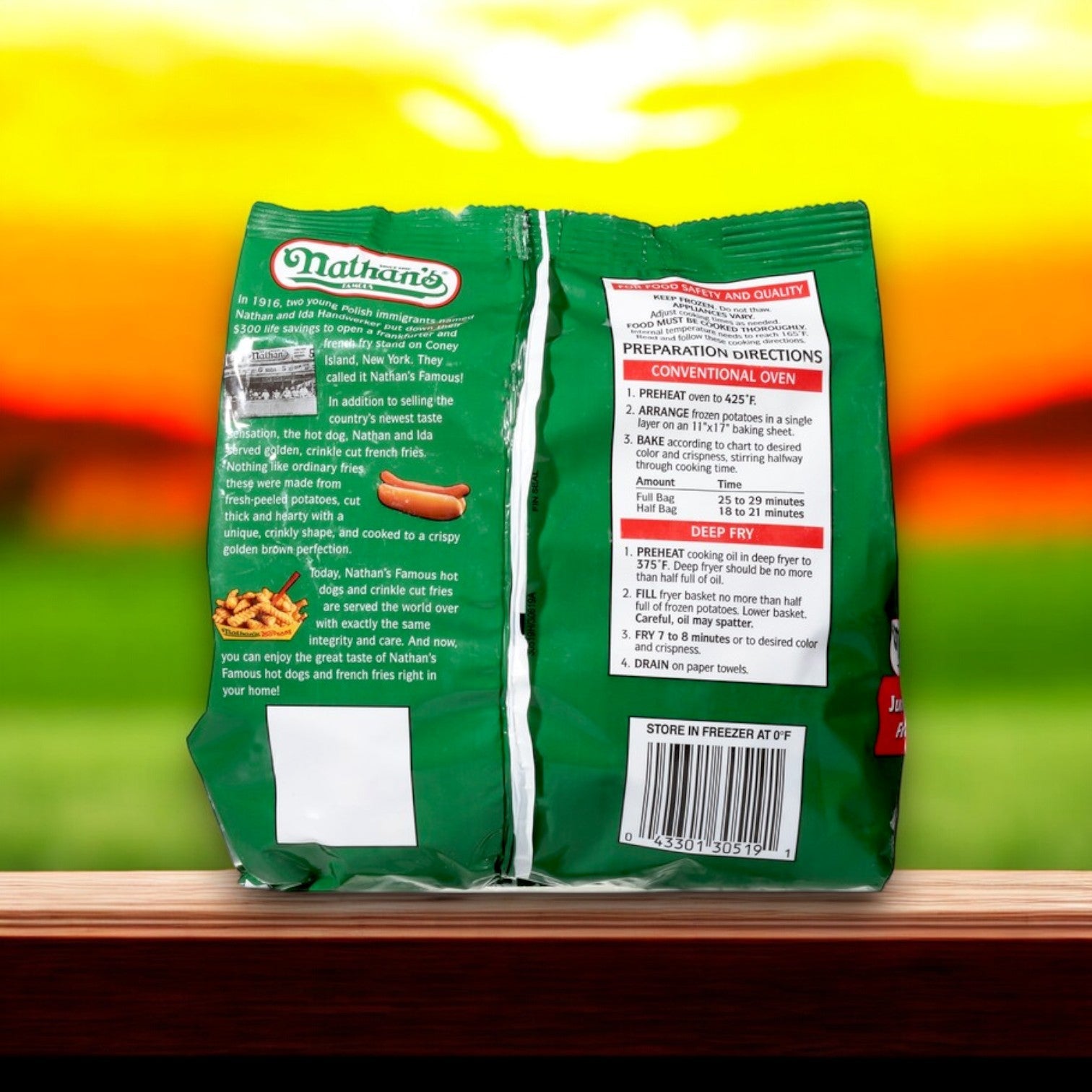 The back of a green Nathan's Famous French Fries, Crinkle Cut, Jumbo – 28 oz package rests on a wooden surface with preparation directions, set against a blurred sunset and field backdrop, evoking the quality and taste synonymous with Nathan’s Famous brand.