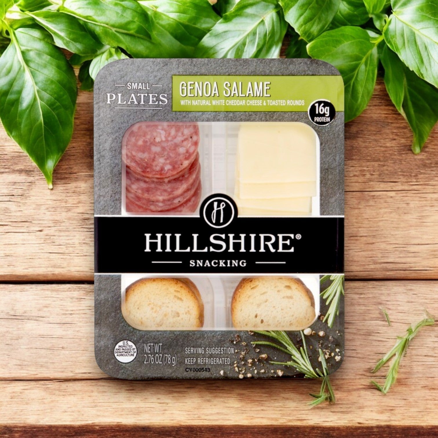Hill Shire's Hillshire Snacking Plates, White Cheddar and Genoa Salame, feature creamy white cheddar and savory Genoa salame stylishly displayed on a wooden surface with green leaves in the background.
