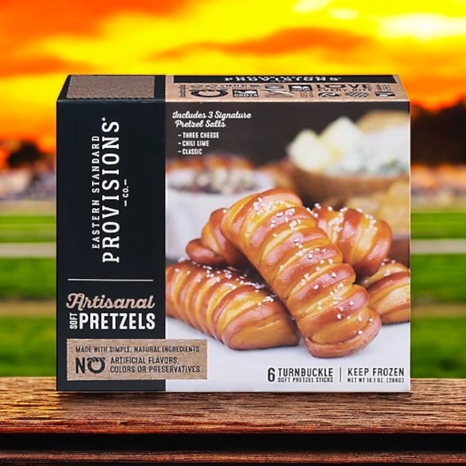 A box of Eastern Standard Provisions Soft Artisanal Turnbuckle Pretzels (6 ct) sits on a wooden surface with a sunset backdrop, highlighting their natural ingredients.