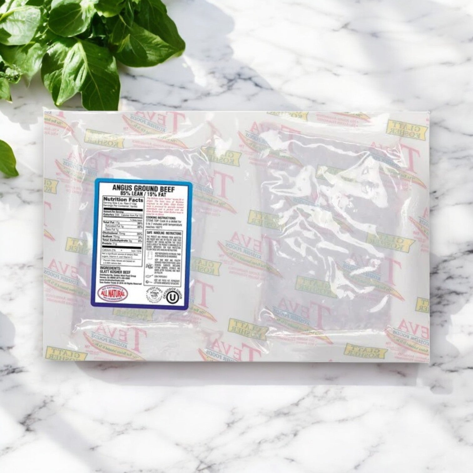 A vacuum-sealed package of Teva Kosher Foods Glatt Kosher Angus Ground Beef, 85% lean, with nutritional facts and certification rests on a marble surface alongside fresh basil leaves.