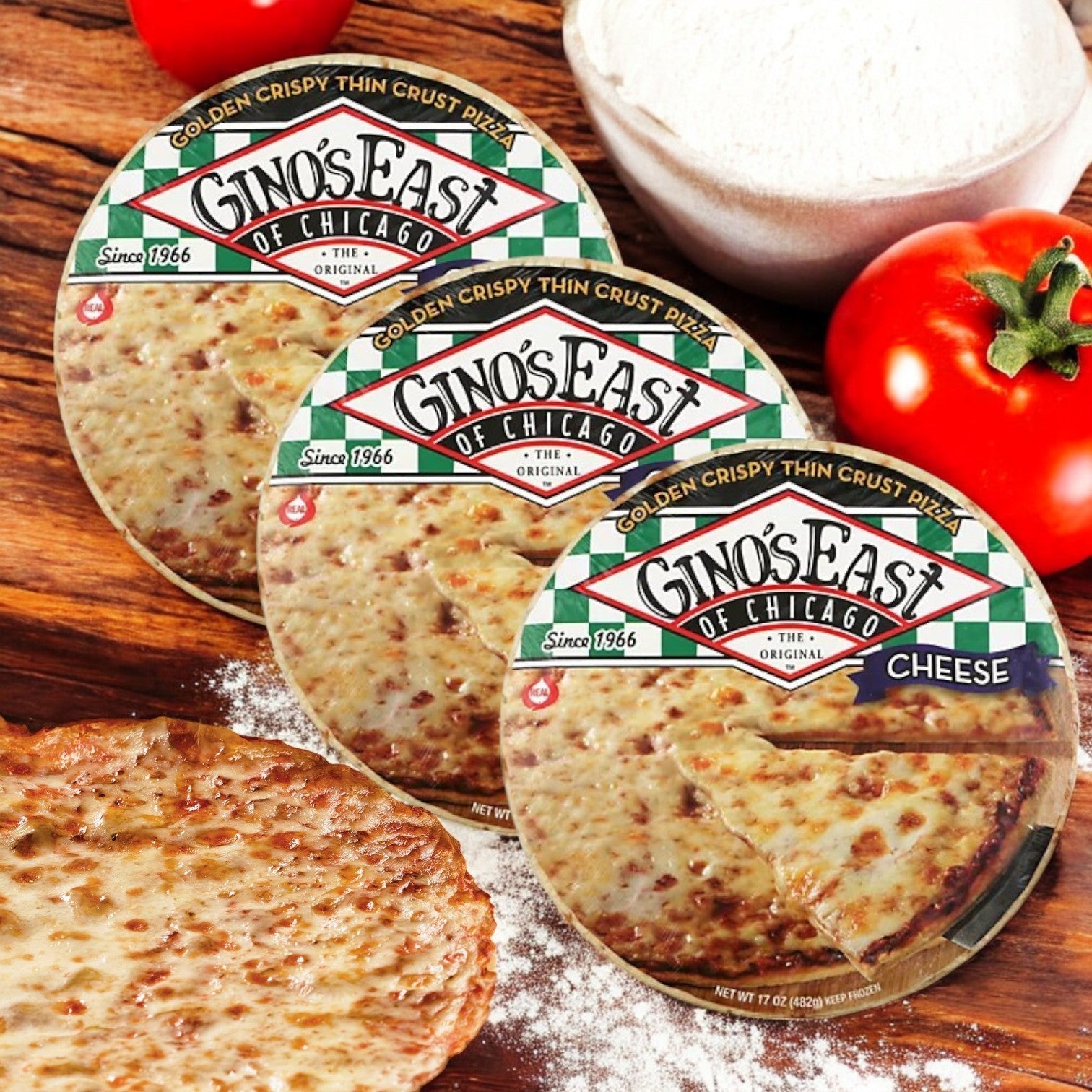 Three Gino's East of Chicago Golden Crispy Thin Crust Pizzas, 15.6 oz each, are displayed on a wooden surface with ripe tomatoes and an unwrapped pizza, highlighting their delicious thin crust and flavors.