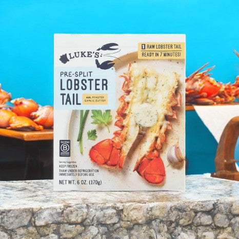 Visual of Luke's Lobster Pre-Split Lobster Tail With Roasted Garlic Butter packaging on stone, accompanied by a cooked lobster on wood, drizzled in roasted garlic butter.