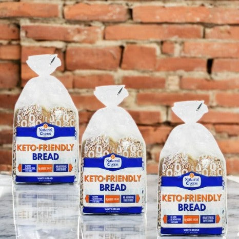 Natural Oven's Keto Friendly Bread-3 Count is displayed in plastic packaging on a marble surface against a red brick wall—ideal for anyone seeking delicious low-carb bread from Natural Oven's.
