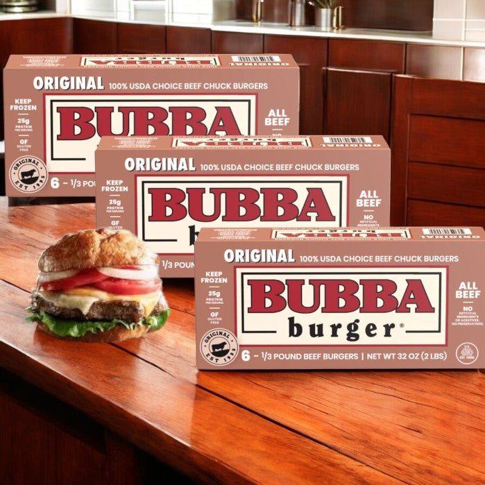 Three boxes labeled "Bubba Burger Original- 6 Count Frozen - 32 Oz- 3 Pack" are on a wooden counter beside a cooked burger with lettuce, tomato, and onion. These Bubba frozen burgers offer the ideal mix of convenience and quality.