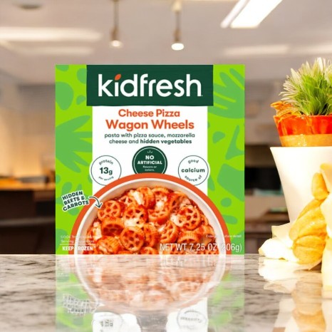 A box of Kidfresh Wagon Wheels Mac & Cheese sits on the counter, showcasing its organic pasta with cheese and pizza sauce noodles, free from artificial flavors and containing hidden vegetables.