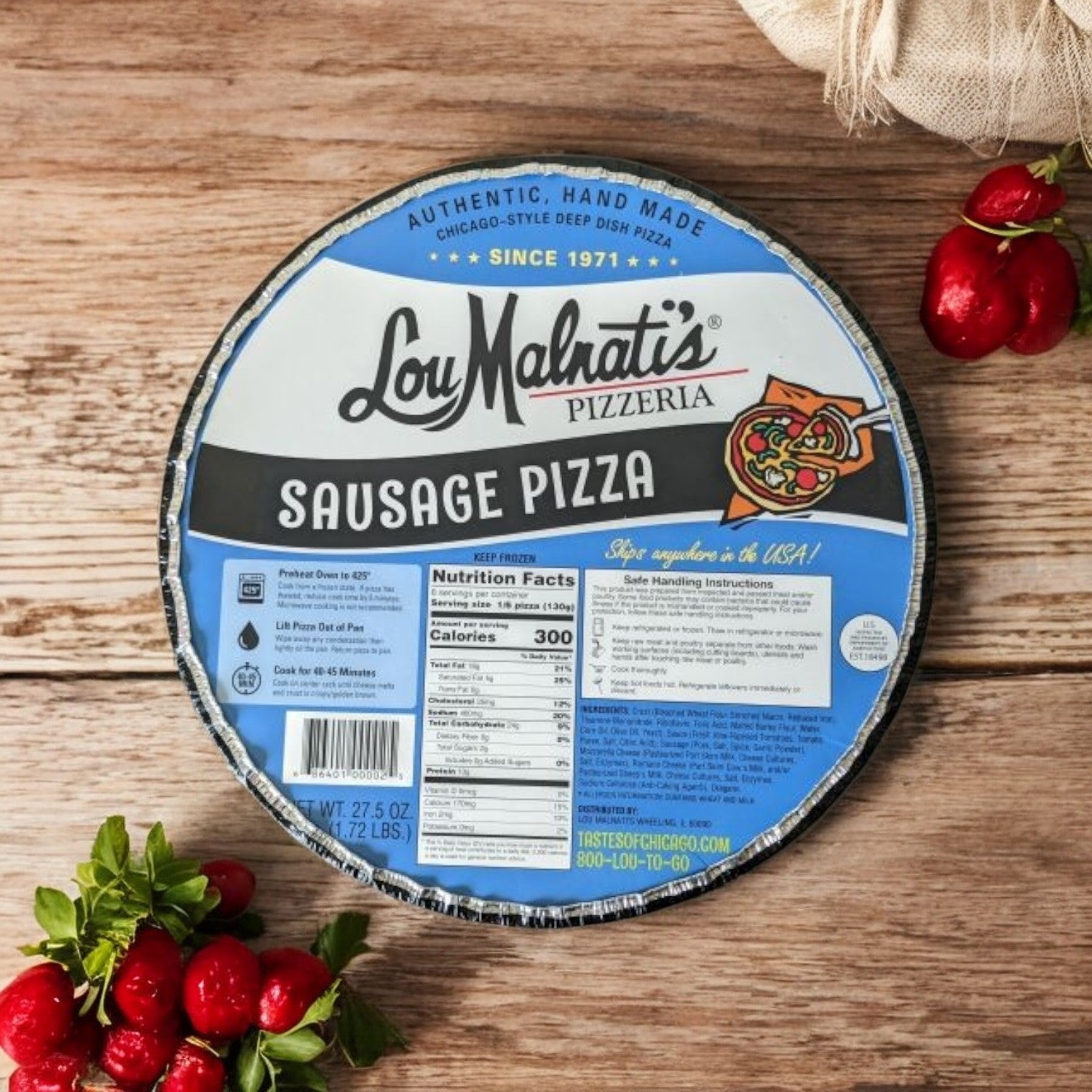 A box of Lou Malnati's Deep Dish Pizza Sausage, 27.5 oz. - 1 Count, sits on a wooden surface amidst fresh tomatoes and herbs, highlighting the rich flavors of Chicago deep dish pizza with its buttery flaky crust and savory Italian sausage from Lou Malnati's.