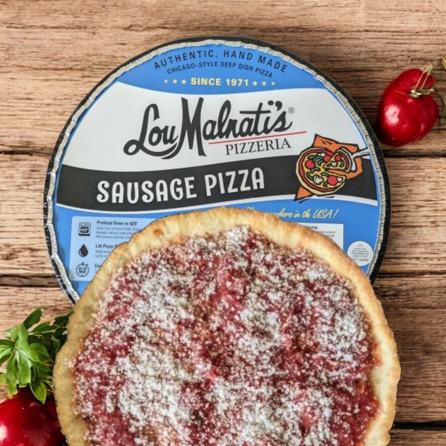 Lou Malnati's Deep Dish Pizza Sausage, weighing 27.5 oz., displays a buttery, flaky crust with its packaging subtly in the background. This Chicago-style deep dish treat is topped with tomato sauce and cheese, resting on a wooden surface and garnished with red pepper.