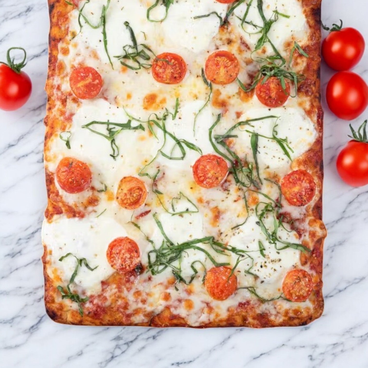 Massa Pizza Co. Margherita Bakery Pizza, 21.6 oz., featuring handcrafted dough topped with mozzarella, sliced tomatoes, and basil on a marble surface. Four whole tomatoes rest on the side.