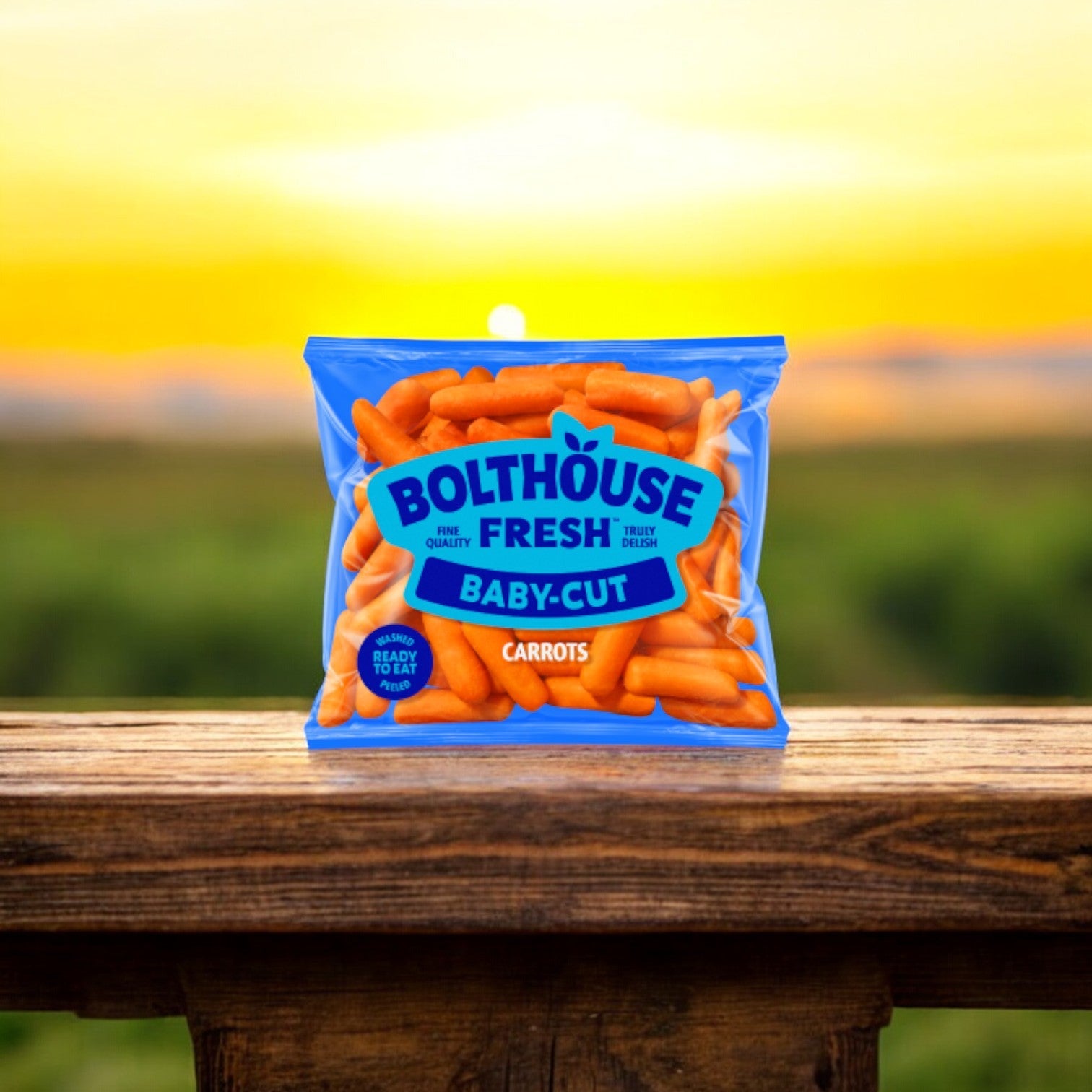 A 1.6 oz. bag of Bolthouse Farms Baby Cut Peeled Carrots sits on a wooden railing, presenting a healthy snack as the sun sets in the blurred background.