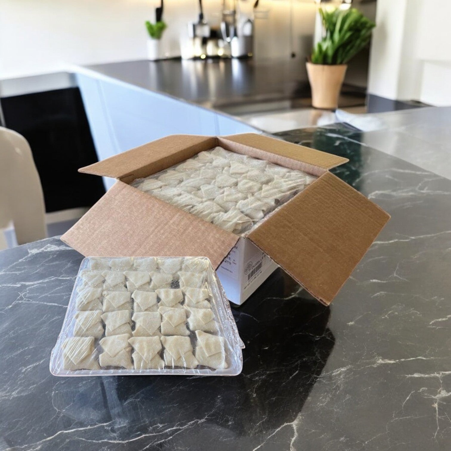 A Sysco cardboard box on a marble countertop holds a tray of wrapped Beef Wellington- Deluxe dumplings from their premium appetizer line. Kitchen utensils and a potted plant create culinary charm in the background.