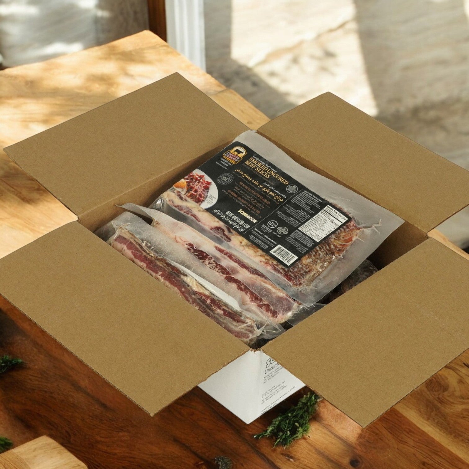 On a wooden table, an open cardboard box reveals vacuum-sealed packs of Certified Angus Beef Bacon Beef Halal Schmacon, showcasing their Halal certification.