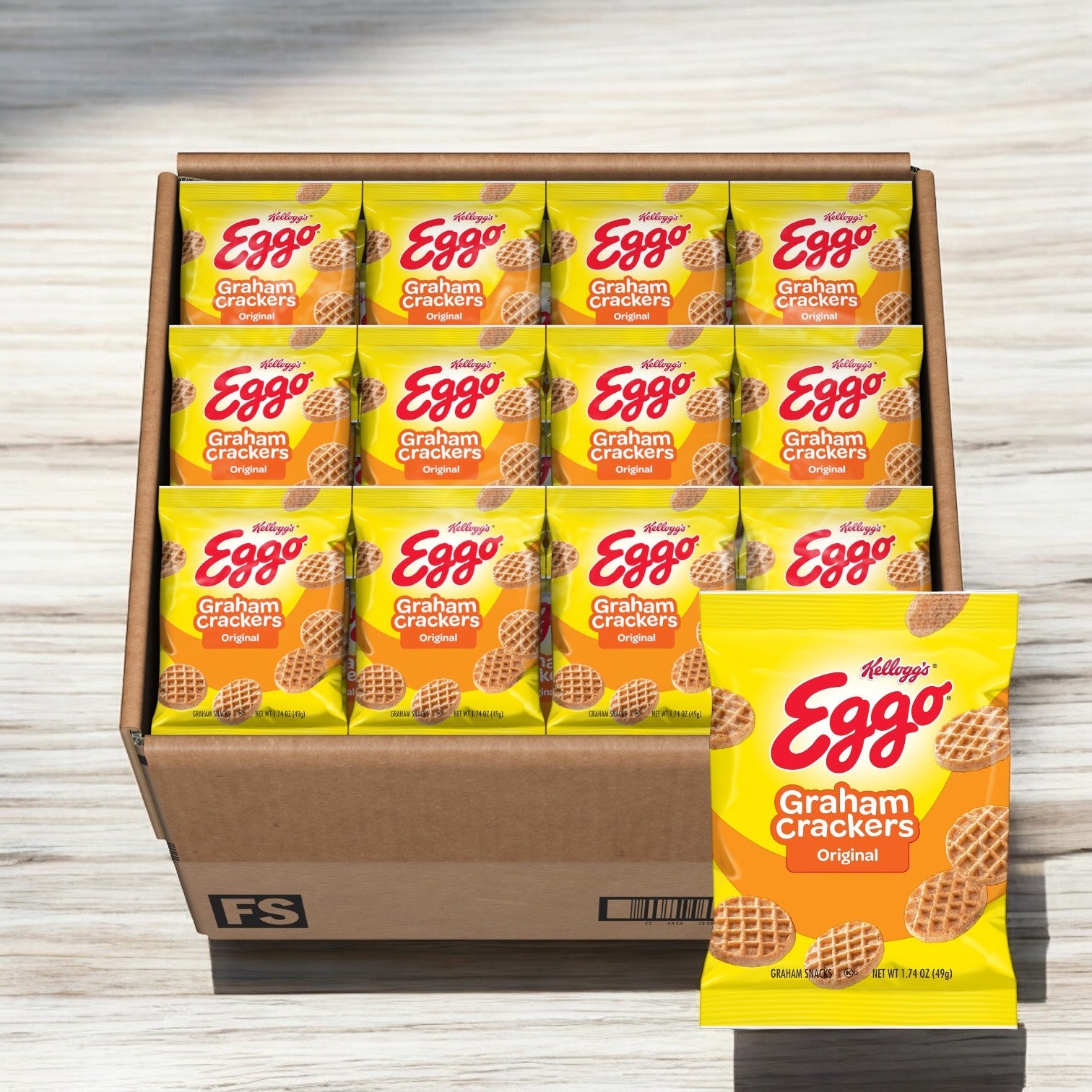 A case of Kellogg's Eggo Graham Cracker Waffles, containing 100 packs, sits on a wooden surface. One pack stands upright in front, highlighting its whole grain goodness.