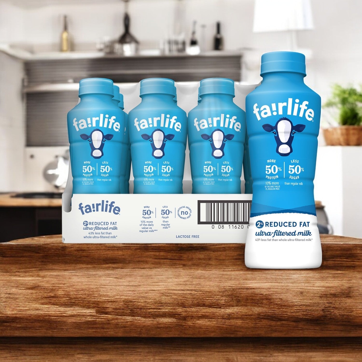 Six bottles of FairLife 2% Ultra-Filtered Reduced Fat Milk from a 12-pack on a wooden surface with a kitchen background, offering high-protein nutrition.