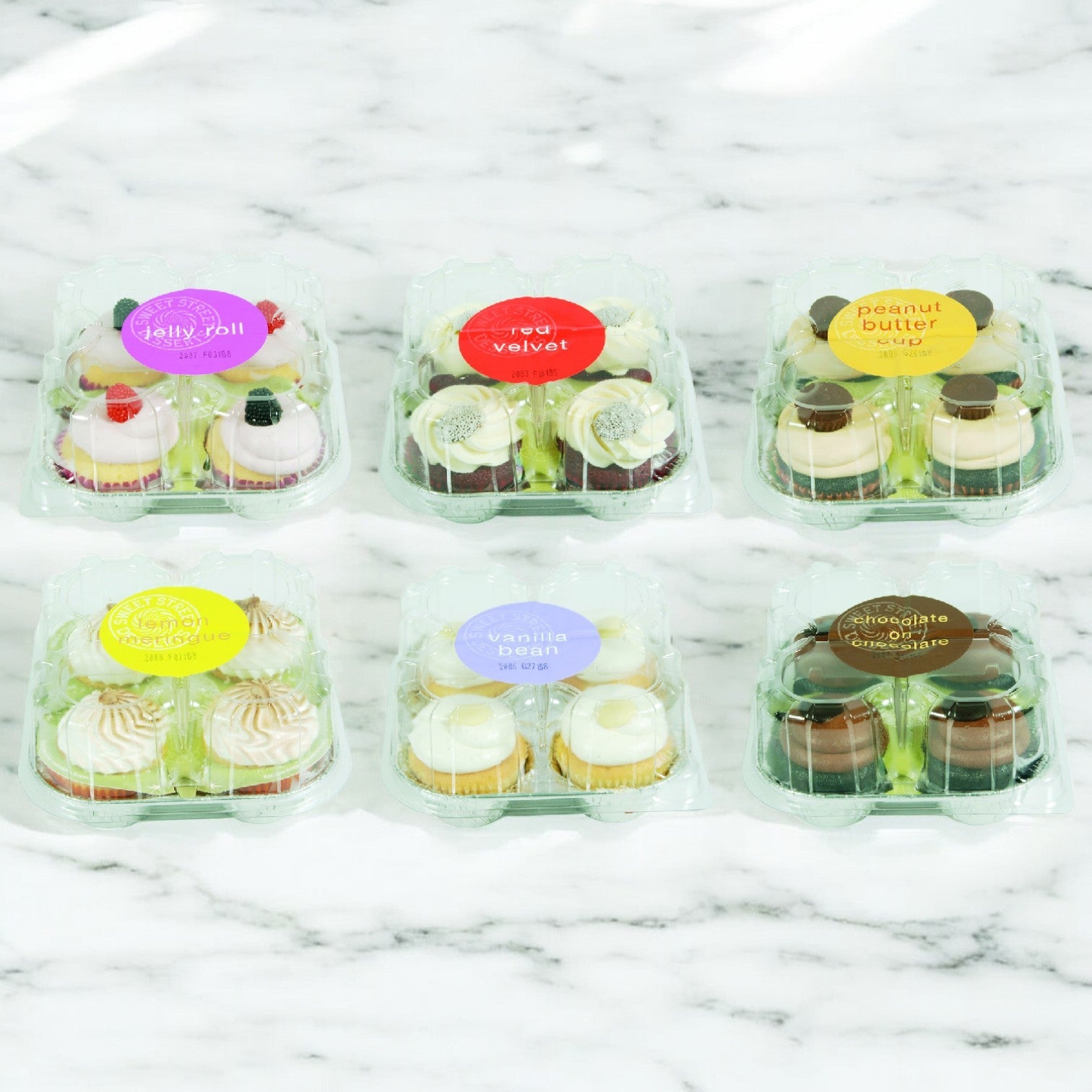 A case of Sweet Street Cupcake Assorted, containing 8 packs and 32 cupcakes in flavors like jelly roll, red velvet, peanut butter, lemon drop, vanilla bean, and chocolate creme, sits enticingly on a marble surface.