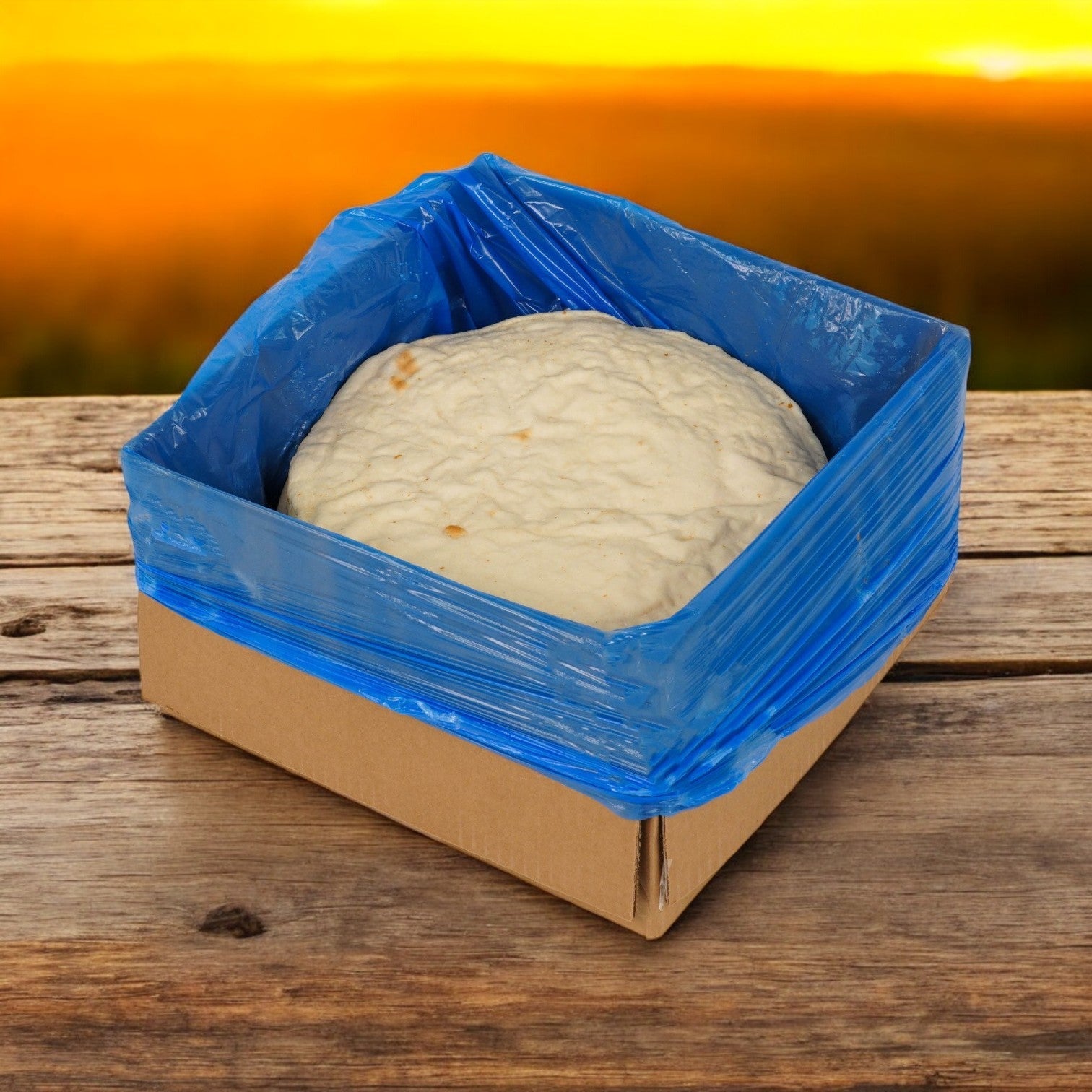 A Venice Bakery 12" Prebaked Gluten-Free Pizza Crust (Frozen) from Venice Baking Co. sits in a cardboard box lined with a blue plastic bag, displayed on a wooden surface. Each case includes 20 crusts.