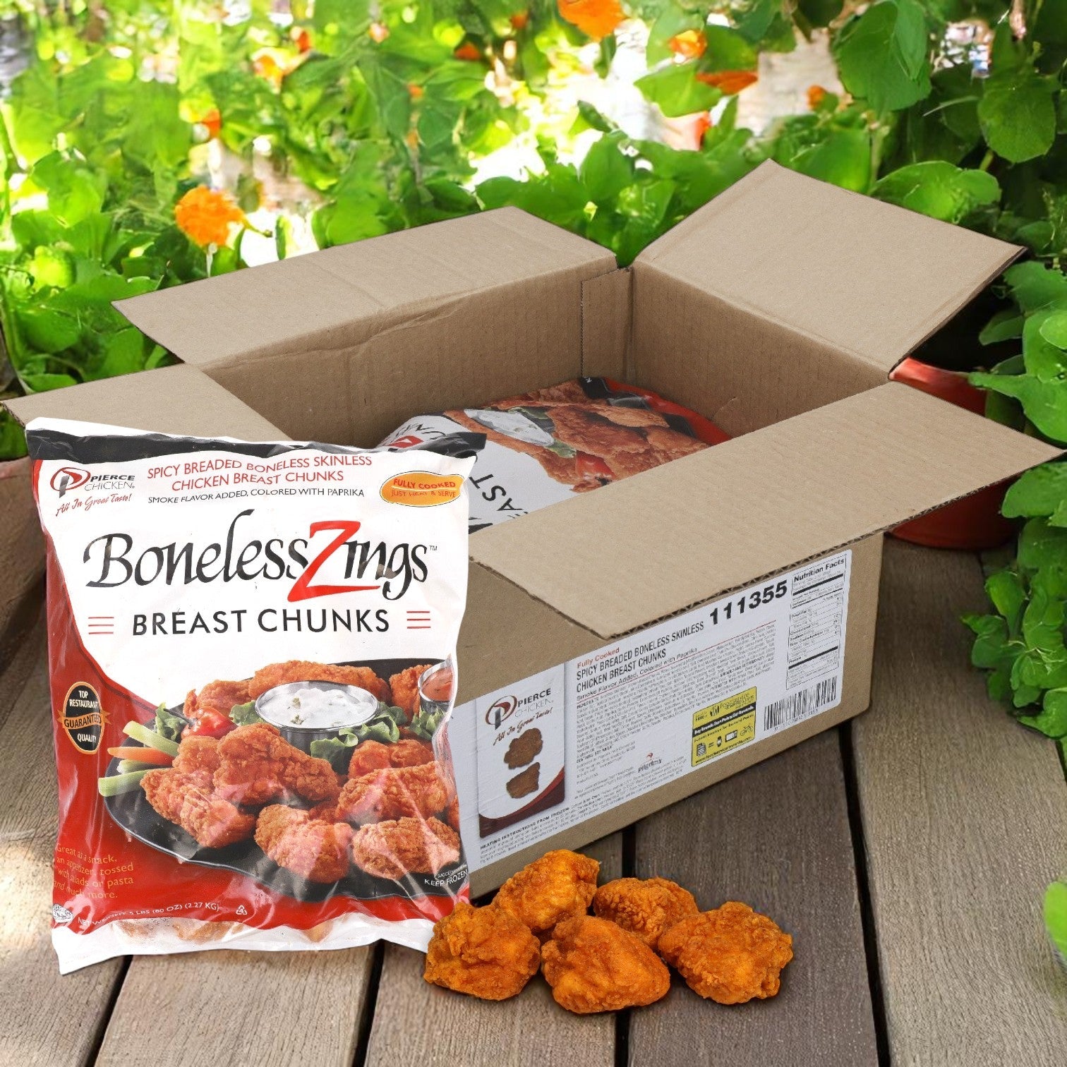 A package of Pierce Boneless Zing Chicken Wings, Breaded & Precooked (2/5 LB bags), sits by an open box with more bags inside on a wooden surface, orange flowers in the background.