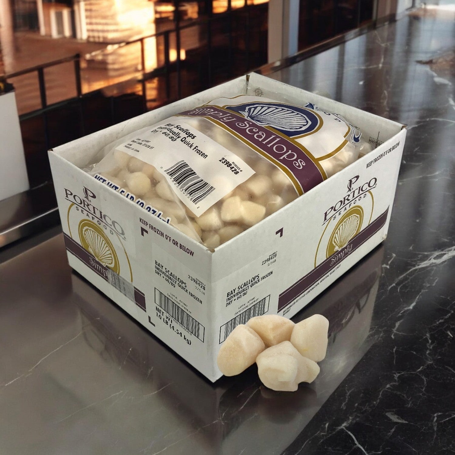 A box of Portico Classic Seafood's Scallop IQF Dry, with 60-80 count imported scallops, sits on a black marble counter, its packaging partially open to reveal the pristine sea scallops inside.