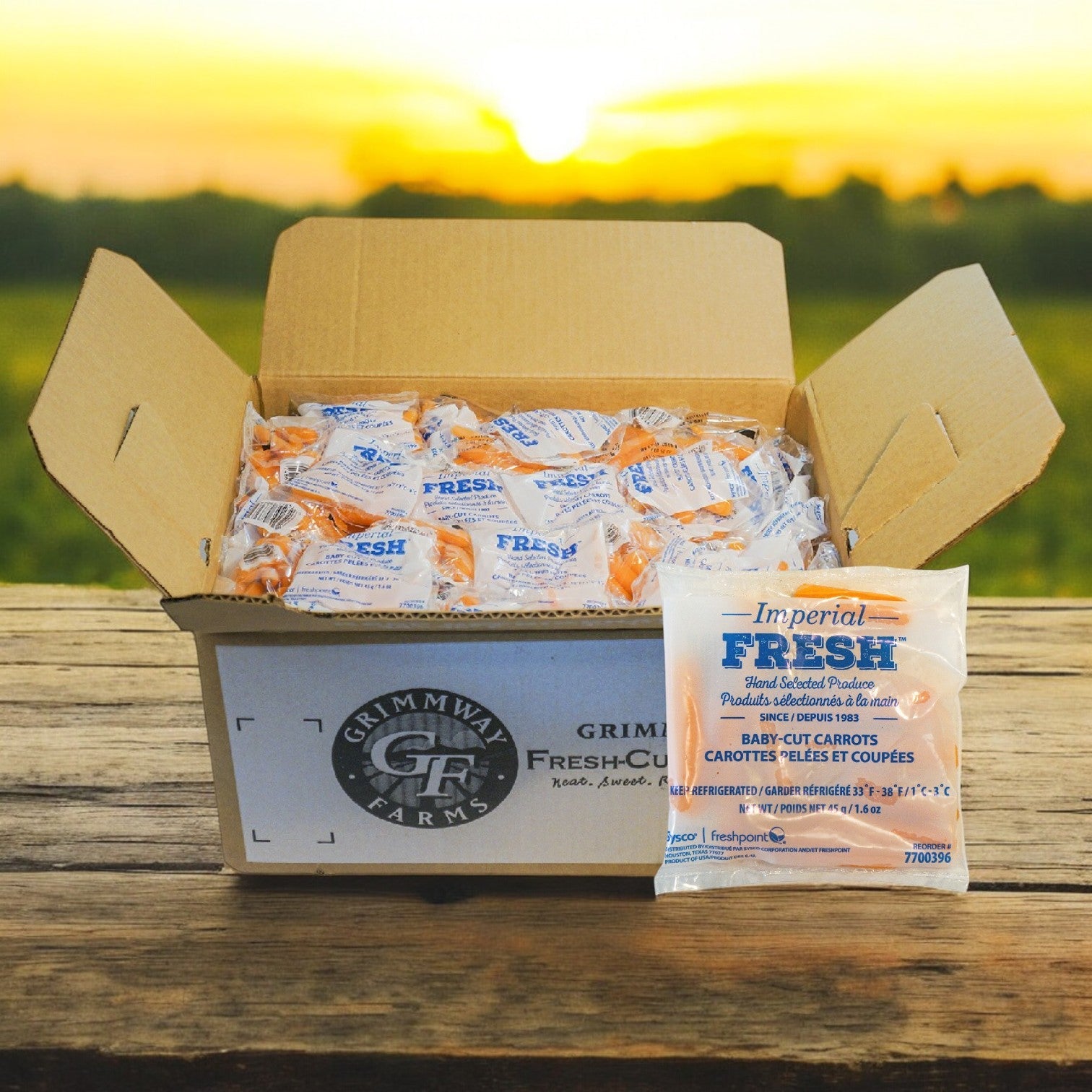 A bulk pack of Sysco Baby Carrots in Bags—Cut, Peeled 1.6 oz., 200 bags—is displayed on a wooden surface outdoors at sunset, offering a convenient and healthy snack option.
