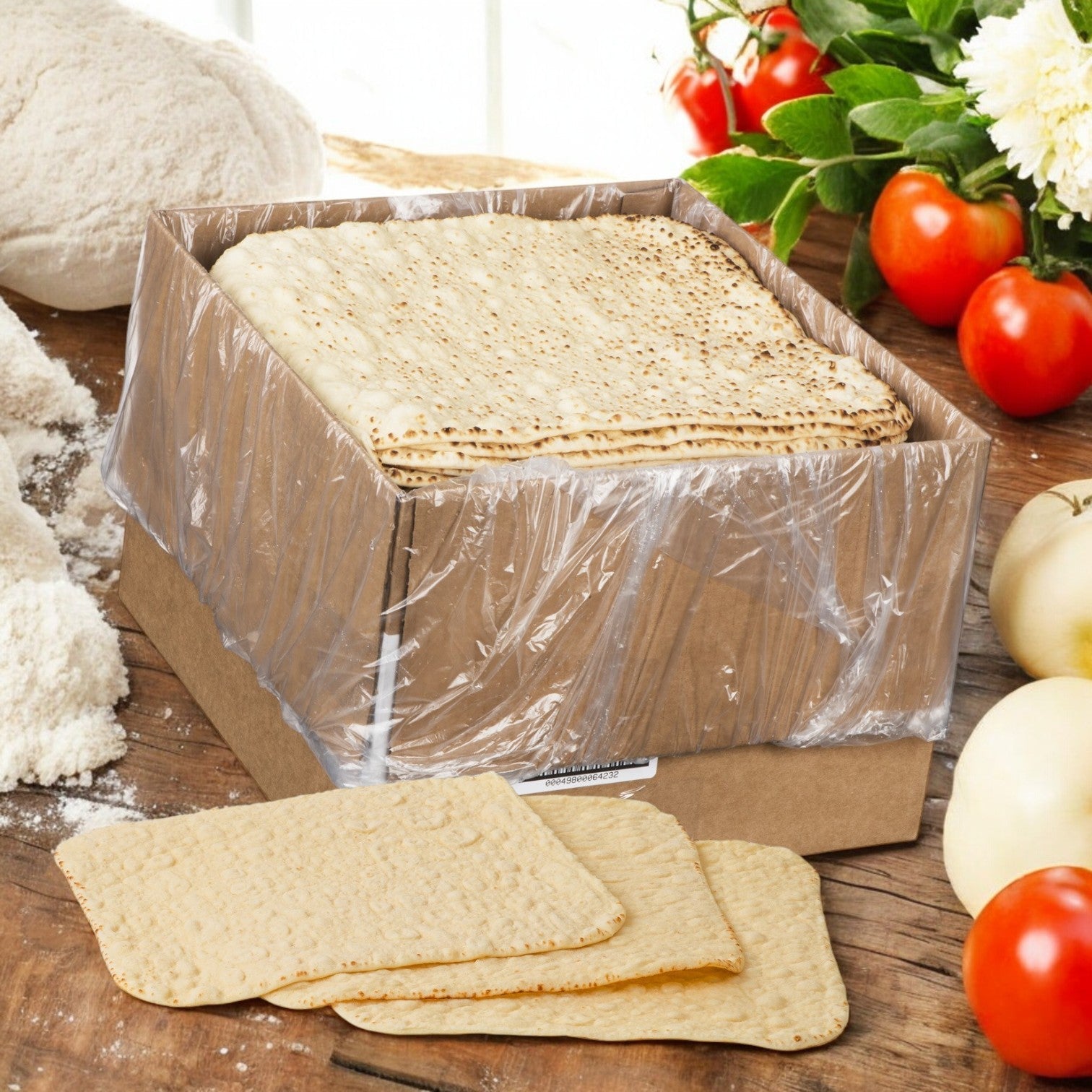 A box of Rich’s Bread Flat Thin Oven Fired 12" X 12", partially wrapped in plastic, is nestled among flour, dough, tomatoes, and onions on a rustic wooden surface.