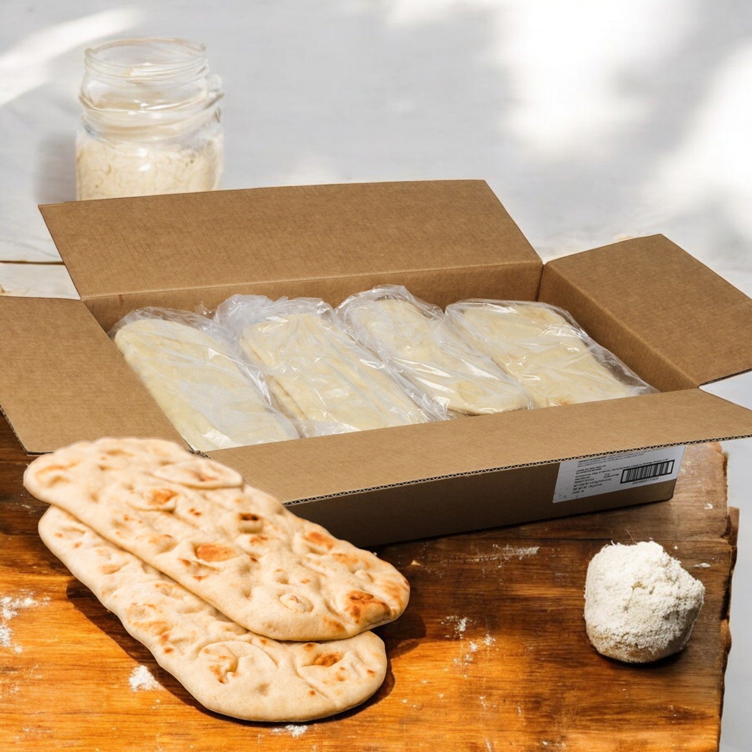 Rich's Bread Flat Oval 12" X 5", 48/4.8oz displayed with two flatbreads and dough on a wooden surface, flour jar in the back.