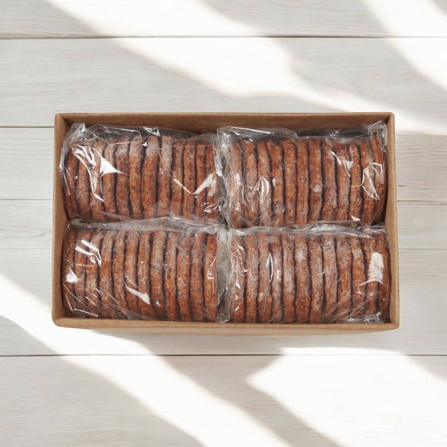 A box with round cookies, in four clear plastic-wrapped sections, sits on a light wooden surface next to a Morning Star Farms Garden Burger (Morningstar Farms Vegetarian Patty Garden Burger 48/3.5 OZ).