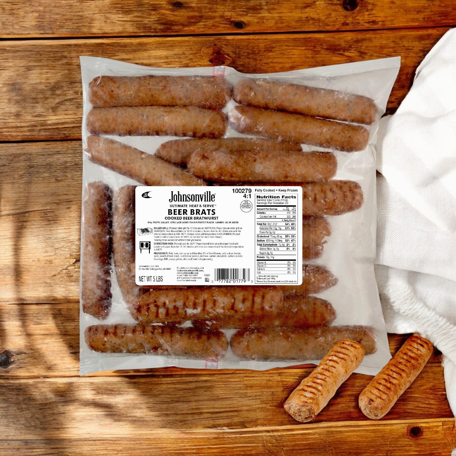 A sealed package of Johnsonville Foods Bratwurst 4 Per # Beer Ultimate (2/5 LB), crafted by the Johnsonville brand, rests on a wooden surface with a white napkin nearby.