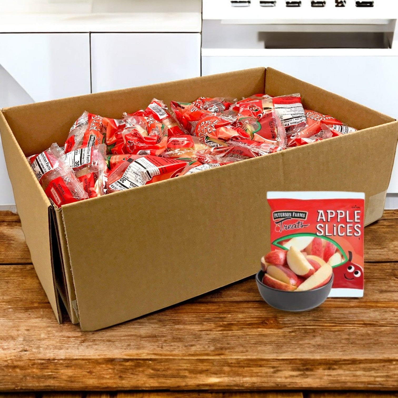 A large cardboard box labeled "Fresh Sliced Apple Packs for Convenient Snacking, 2 oz. -1 Cases- Bulk 100" by Peterson Farms sits on a wooden surface. One package shows apple slices in a bowl, promoting these healthy snacks.