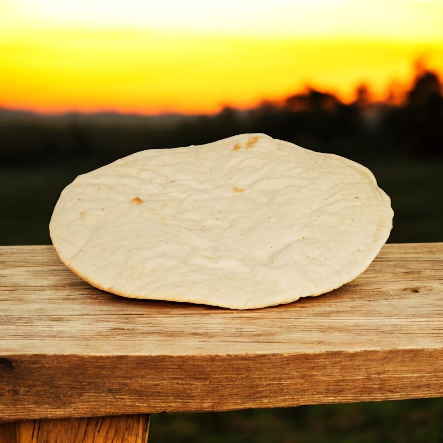 A Venice Bakery 12" Prebaked Gluten-Free Pizza Crust from Venice Baking Co. (Frozen, 20 per case) sits round and ready on a wooden surface outdoors, framed by a sunset and a softly blurred landscape in the distance.