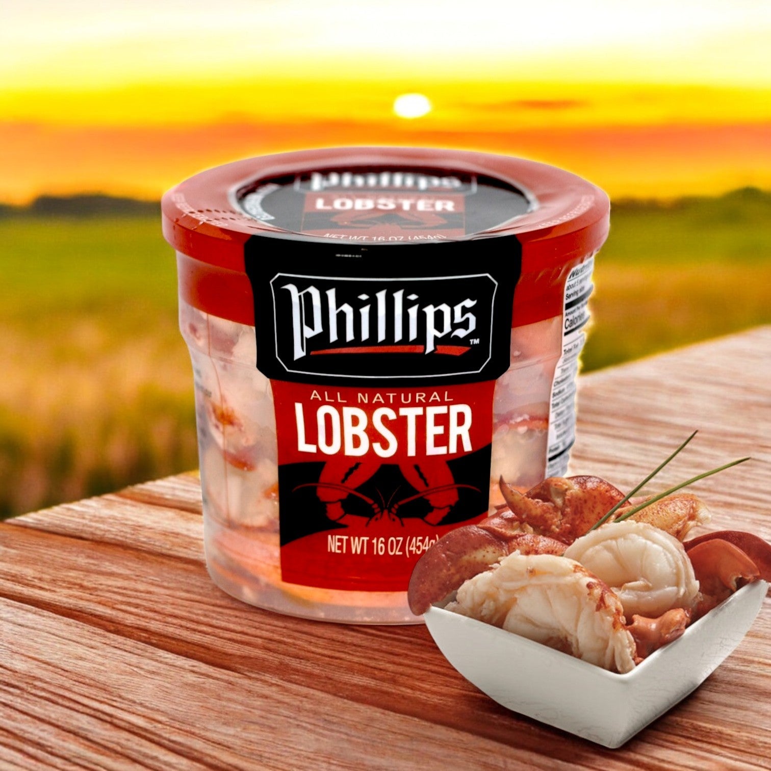 A sunset over a field forms the backdrop for a container of Phillips Foods Lobster Meat on a table, with seafood in a small dish. This pasteurized lobster's rich flavors are ideal for crafting exquisite coastal-inspired dishes.