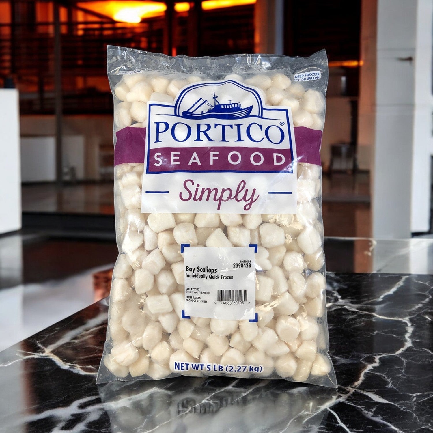 A bag of Portico Classic Seafood Scallop IQF Dry 60-80 Count sits on a marble counter, with transparent packaging featuring a blue logo and purple banner, containing premium quality 2-5 lbs imported scallops that are individually quick frozen.