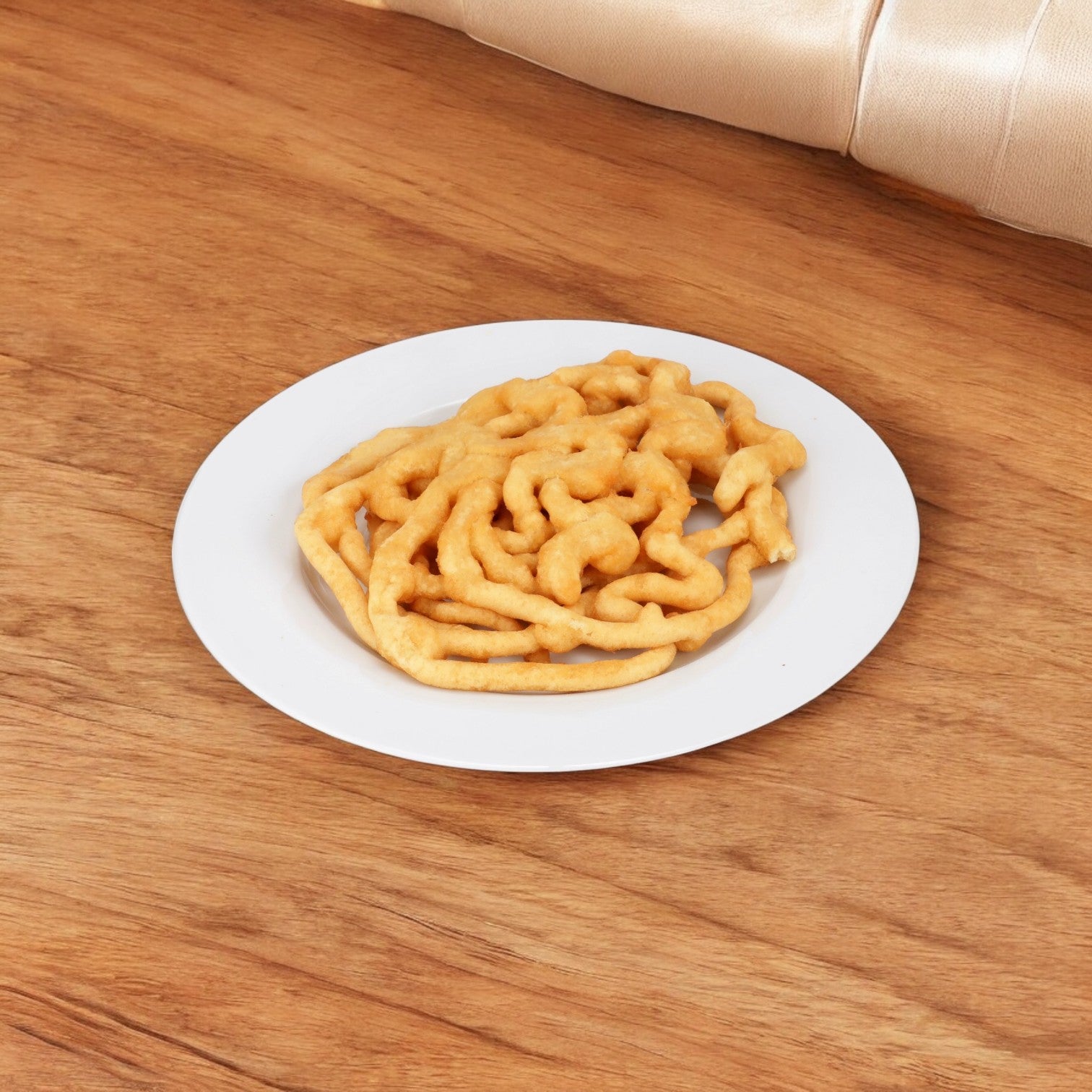 A wooden table holds a white plate topped with a J&J Snacks' Cake Funnel Baked, 8.5 inch, recalling the crispy fried dough treats from concession stands.