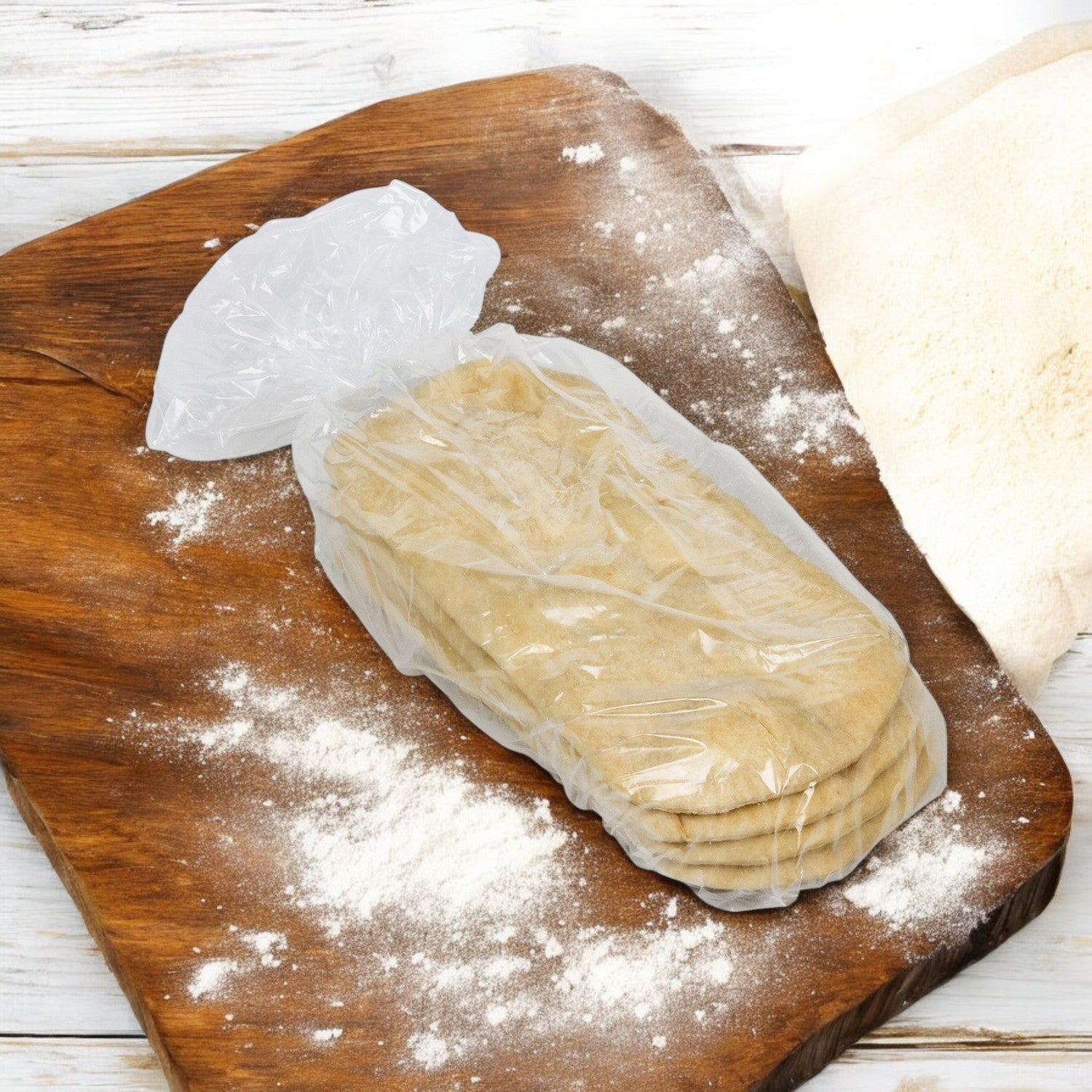 A pack of Rich's Bread Flat Oval 12" X 5", wrapped in plastic, sits on a floured wooden cutting board.