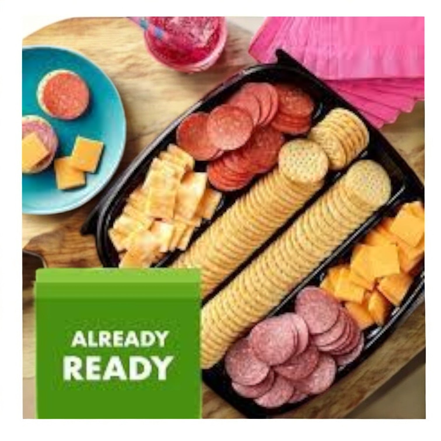 A Hormel Party Tray with crackers, hard salami, pepperoni, and cheese cubes. Nearby is a small plate with similar snacks and a drink. Pink napkins are in the background. The text reads "Already Ready," inviting you to indulge with Hormel's Hard Salami & Pepperoni tray.