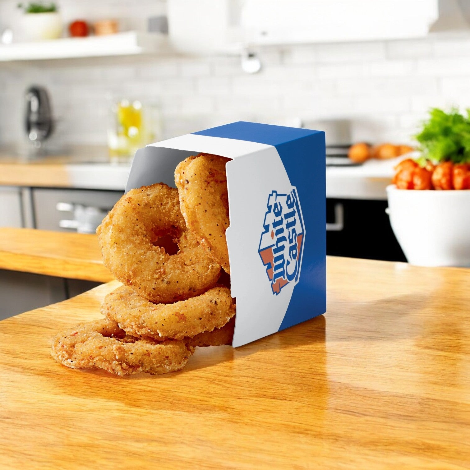White Castle's Original Chicken Rings, in a partially open blue and white box, sit on the wooden kitchen counter, reminiscent of their beloved frozen snacks.