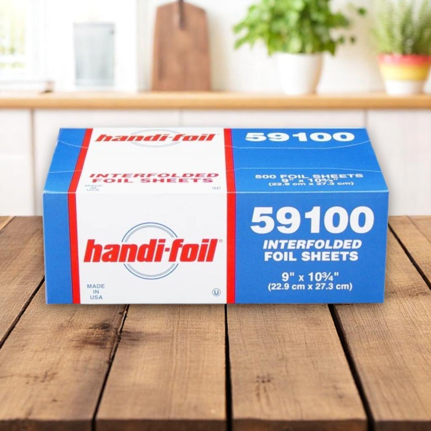 A blue, red, and white Handi-Foil of America box labeled "HFA Pop-Up Foil Sheets – 9\" x 10.75\"" sits on a wooden table in a blurred kitchen, offering 500 convenient pre-cut sheets per pack—perfect for any commercial kitchen.