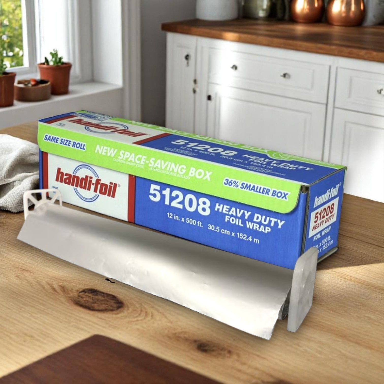 A box of Handi-Foil of America HFA Commercial Heavy Foil Roll, 12" wide and 500 feet long, sits on a kitchen counter with the aluminum foil partially unrolled and the cutting edge visible.