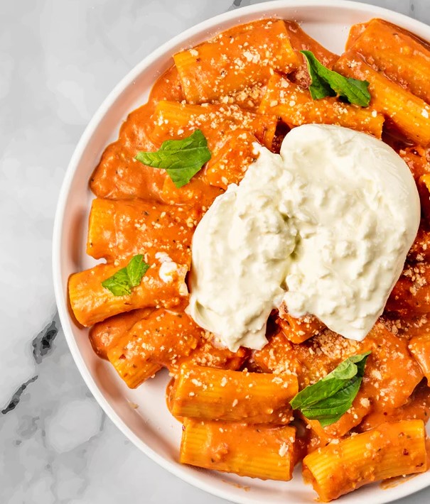 A serving of FoodHaul Spicy Rigatoni, featuring a creamy tomato sauce, topped with burrata cheese and garnished with fresh basil leaves.