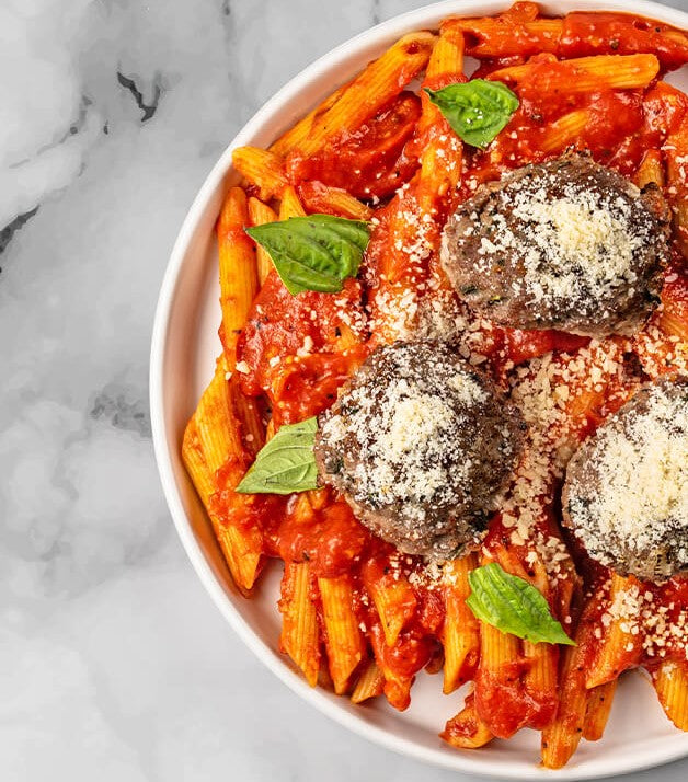 Savor the gourmet experience with FoodHaul's Wagyu Penne With Meatballs, featuring penne pasta draped in a rich tomato sauce, complemented by premium Wagyu beef meatballs, grated cheese, and fresh basil leaves.